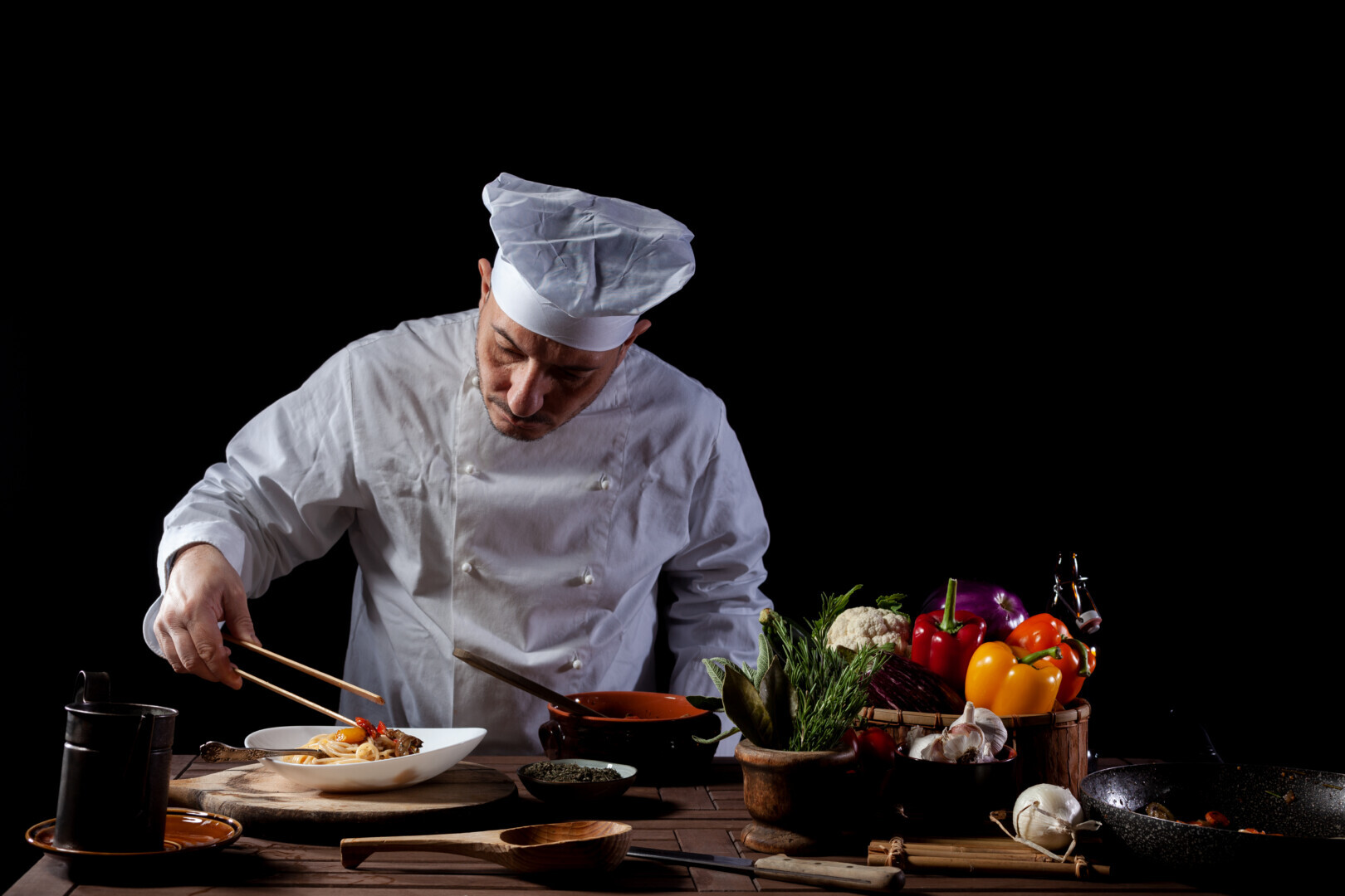 Male Chef In White Uniform Prepares Spaghetti With Vegetables On
